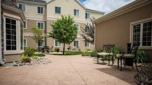 A courtyard with a tree, outdoor seating, and a building with multiple windows. - 1 Bedroom | Free Breakfast (Fargo)