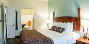 A hotel room with a bed, a nightstand, a lamp, and a door leading to a bathroom. - 1 Bedroom | Free Breakfast (Fargo)