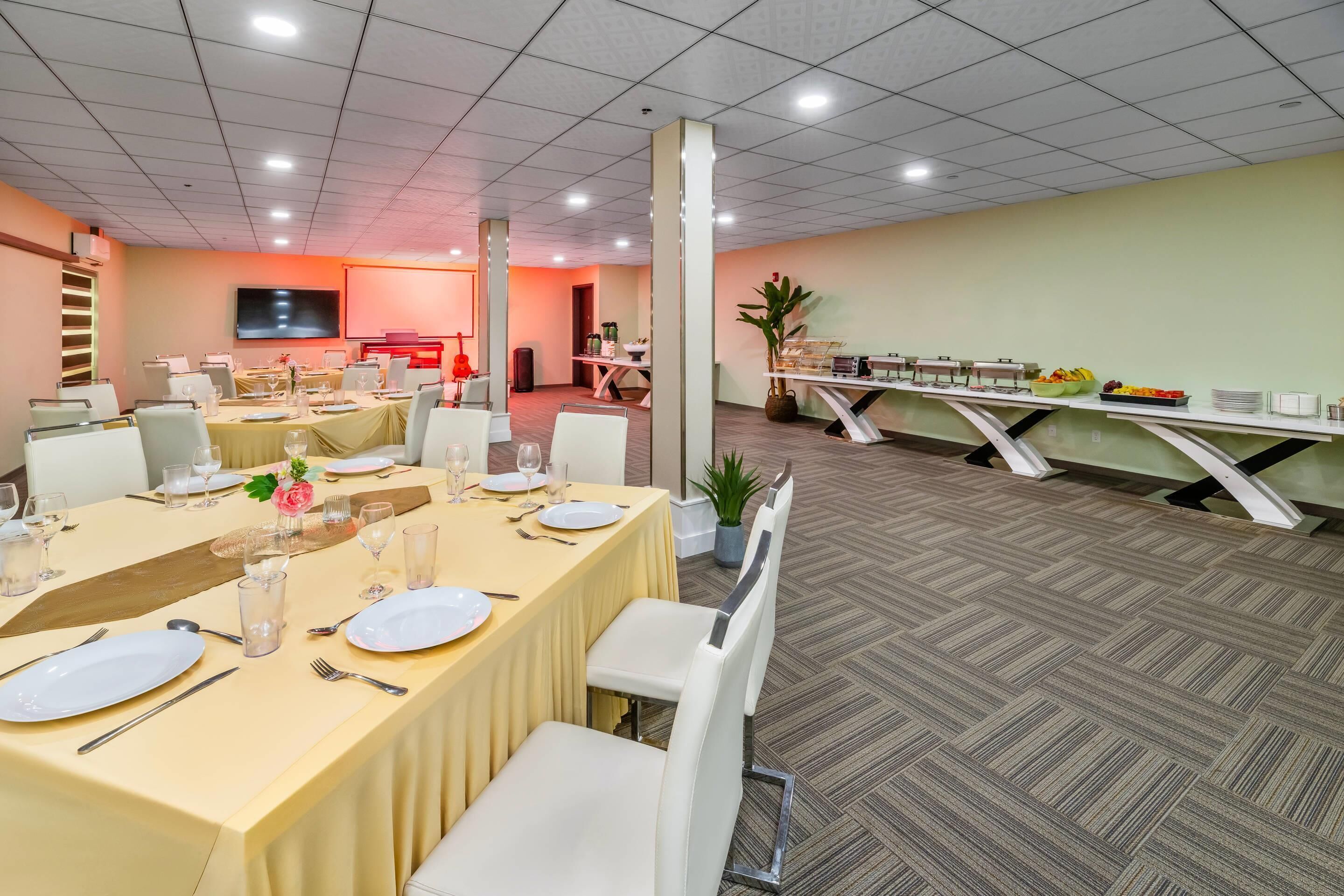 A conference room with tables set for a meeting, equipped with laptops, and a buffet area with fruits and dishes.