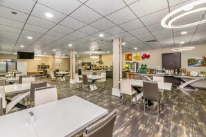 A spacious cafeteria with multiple tables and chairs, a kitchen area, and various food and beverage stations.