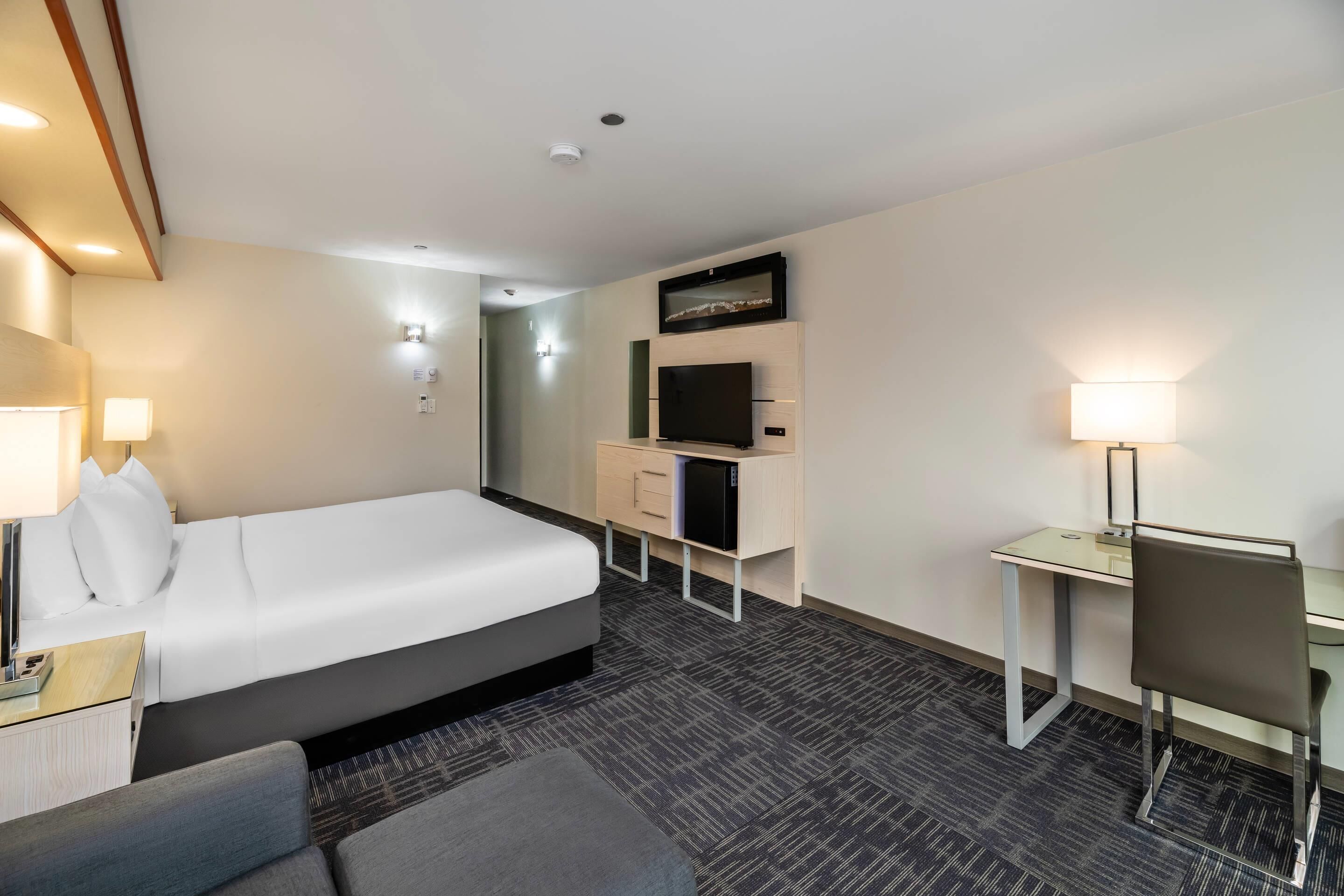 A hotel room with a bed, desk, chair, TV, and lamp.