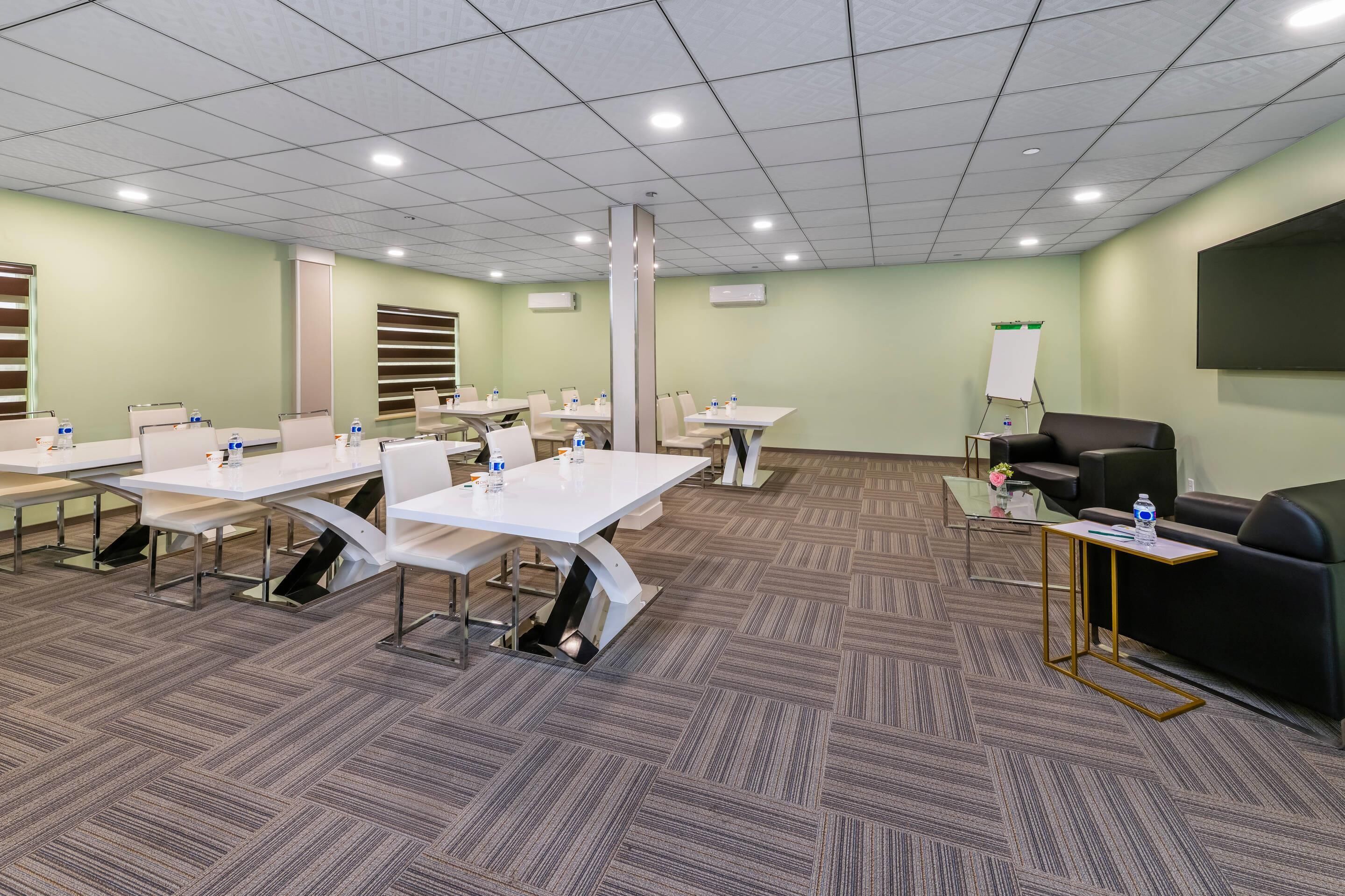 A conference room with tables, chairs, a whiteboard, and a screen.