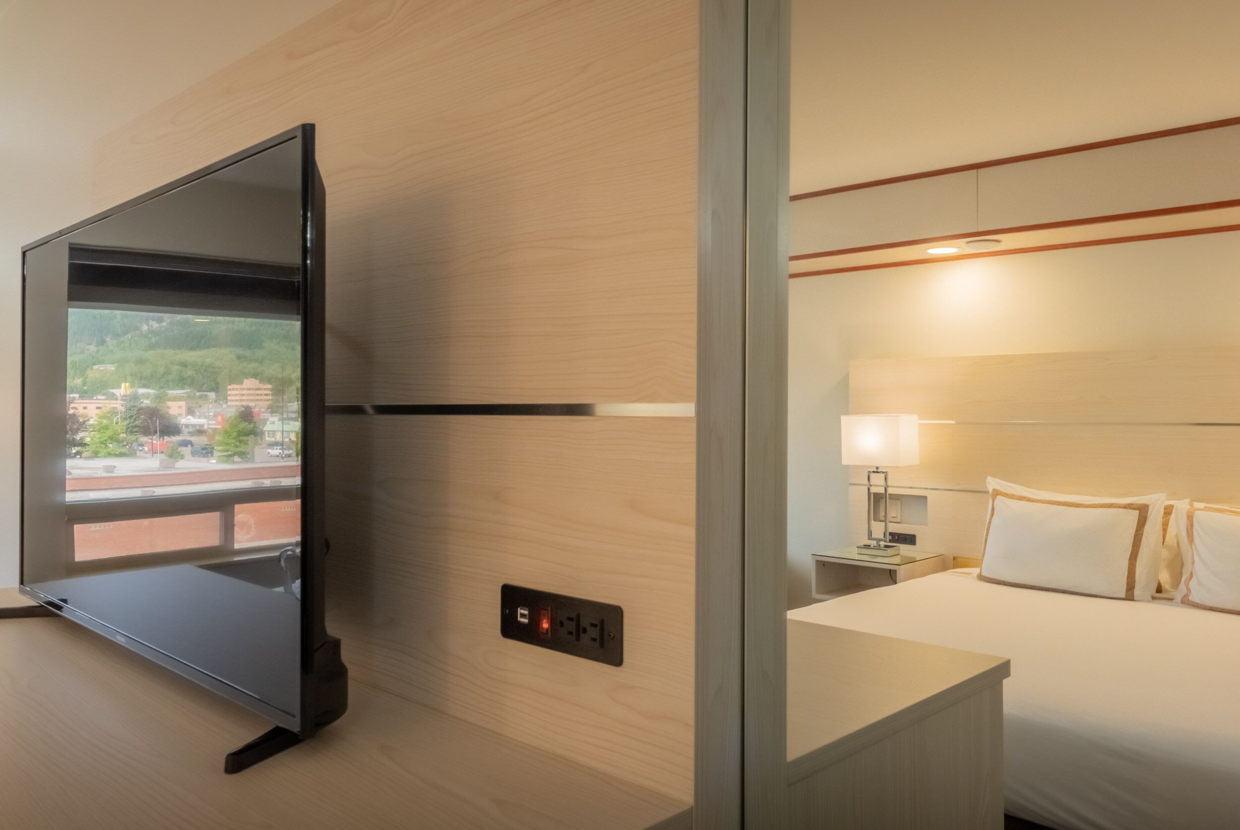 Una habitación de hotel con cama, mesita de noche, lámpara y televisión montada en la pared.