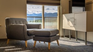 Ein modernes Zimmer mit einem grau gepolsterten Sessel und Hocker, einer Holzkabine und einem großen Fenster mit Blick auf die Berge.