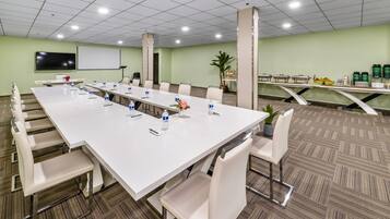 Een vergaderruimte met een lange tafel, stoelen, een scherm voor een beamer en een buffetgedeelte met eten en drinken.