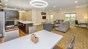 Eine moderne Küche mit Kochinsel, ein Essbereich mit weißem Tisch und ein Wohnbereich mit Sofa und Fernseher.