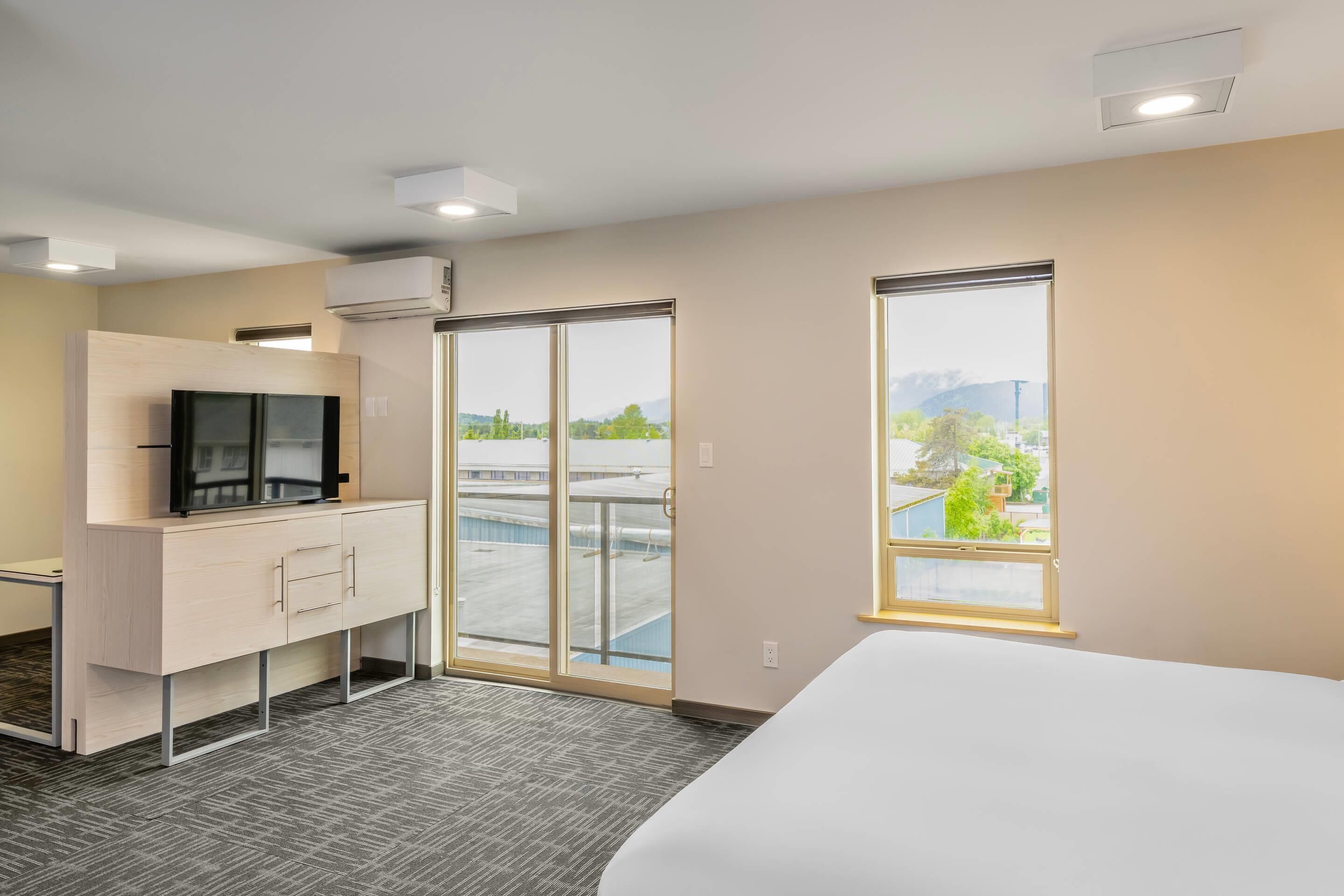 Une chambre d’hôtel avec un lit, un bureau avec une télévision, une porte-fenêtre coulissante donnant sur l’extérieur et une vue sur le paysage urbain.