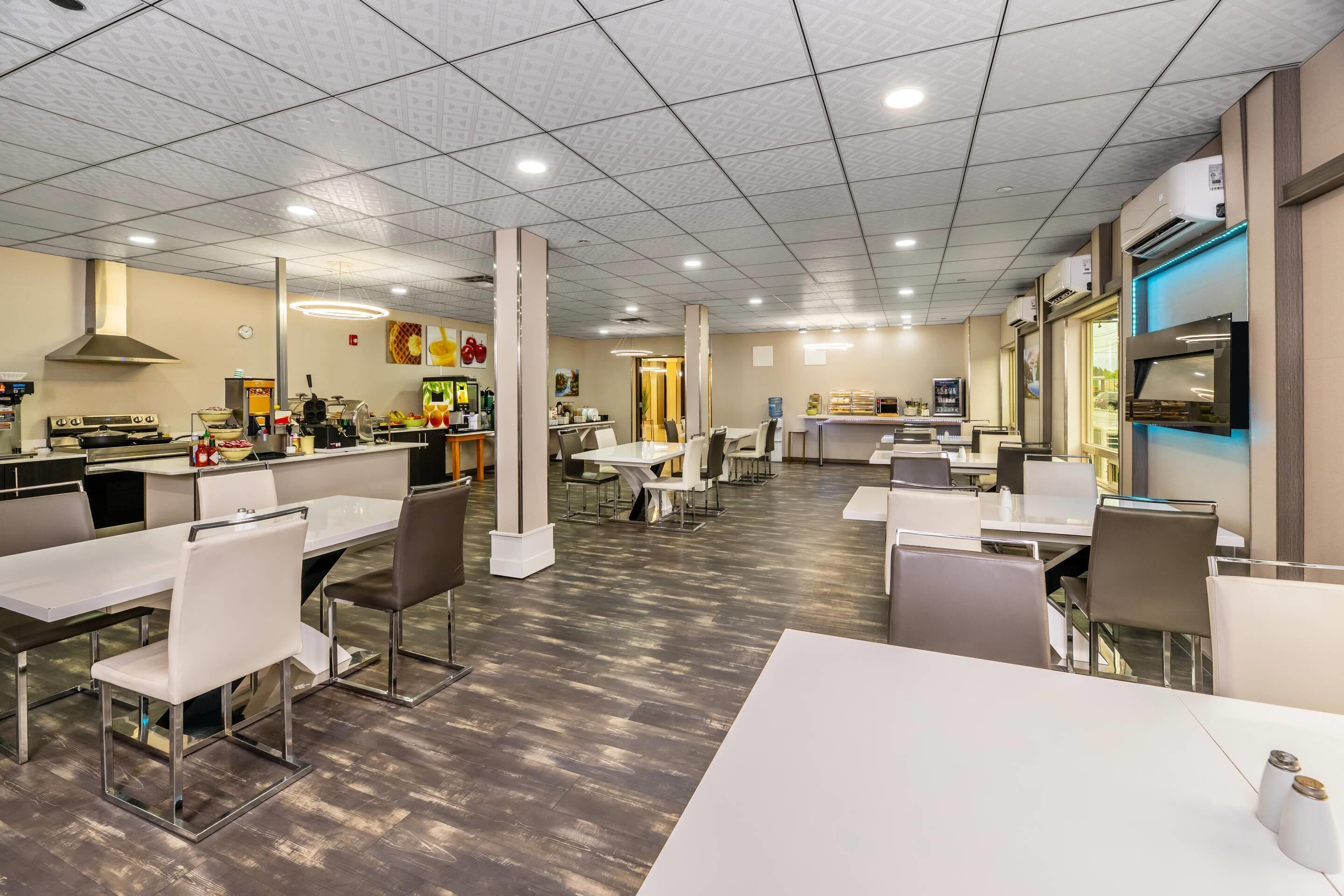 Un grand espace de salle à manger avec plusieurs tables et chaises, une cuisine à l’arrière-plan et un design moderne au niveau du plafond.