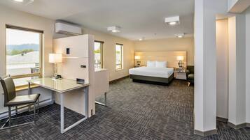 A hotel room with a bed, desk, chair, and a view of the outdoors.
