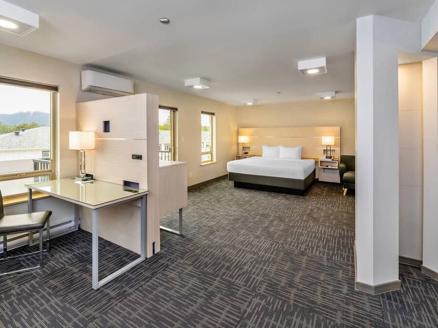 A hotel room with a bed, desk, chair, and a view of the outdoors.