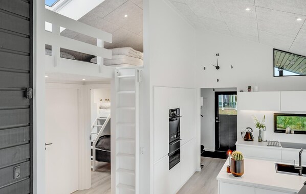 A modern kitchen with built-in appliances, a dining area, and a staircase leading to a loft bedroom.