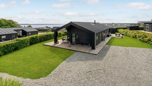 A modern, dark-colored cabin with a covered patio, surrounded by well-maintained lawns and a gravel path. - 3 bedroom stunning home in Haderslev (Haderslev)