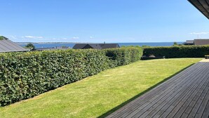 A well-maintained lawn with a wooden deck, a hedge, and a view of the sea and other buildings. - 3 bedroom stunning home in Haderslev (Haderslev)