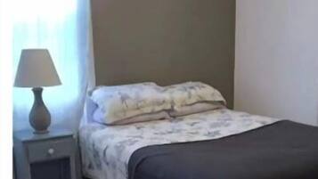 Un dormitorio con cama, mesita de noche, lámpara y ventana con cortinas.