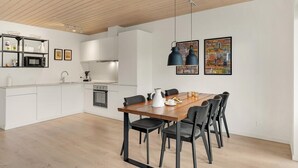 Una cocina moderna con armarios blancos, una mesa de comedor de madera con sillas negras y dos lámparas colgantes.