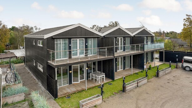Una casa moderna de dos pisos con ventanas amplias, un balcón y un jardín.