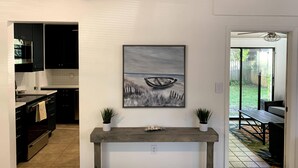 A modern kitchen with dark cabinets, a wooden console table, and a painting of a boat on a beach. - Charming Updated & Pet-Friendly Ranch Close to Beaches, Baseball, and Downtown  (Sarasota)
