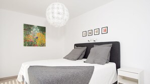 A modern bedroom with a large bed, a white nightstand, a decorative chandelier, and a colorful painting on the wall. - Blue Pearl 206 by Avecoeur (Nice)
