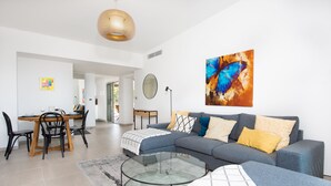 A modern living room with a grey sofa, a glass coffee table, and a dining area with a wooden table and chairs. - Blue Pearl 206 by Avecoeur (Nice)