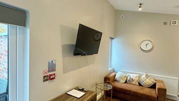 A modern living room with a wooden desk, a brown sofa, a mounted TV, and a window with a view of a brick building.