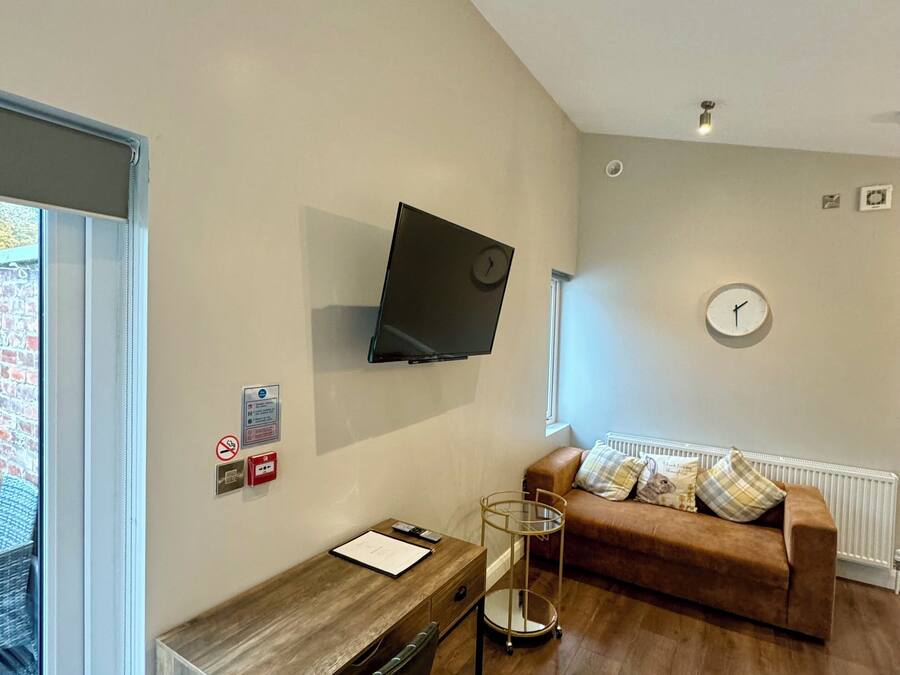 A modern living room with a wooden desk, a brown sofa, a mounted TV, and a window with a view of a brick building.