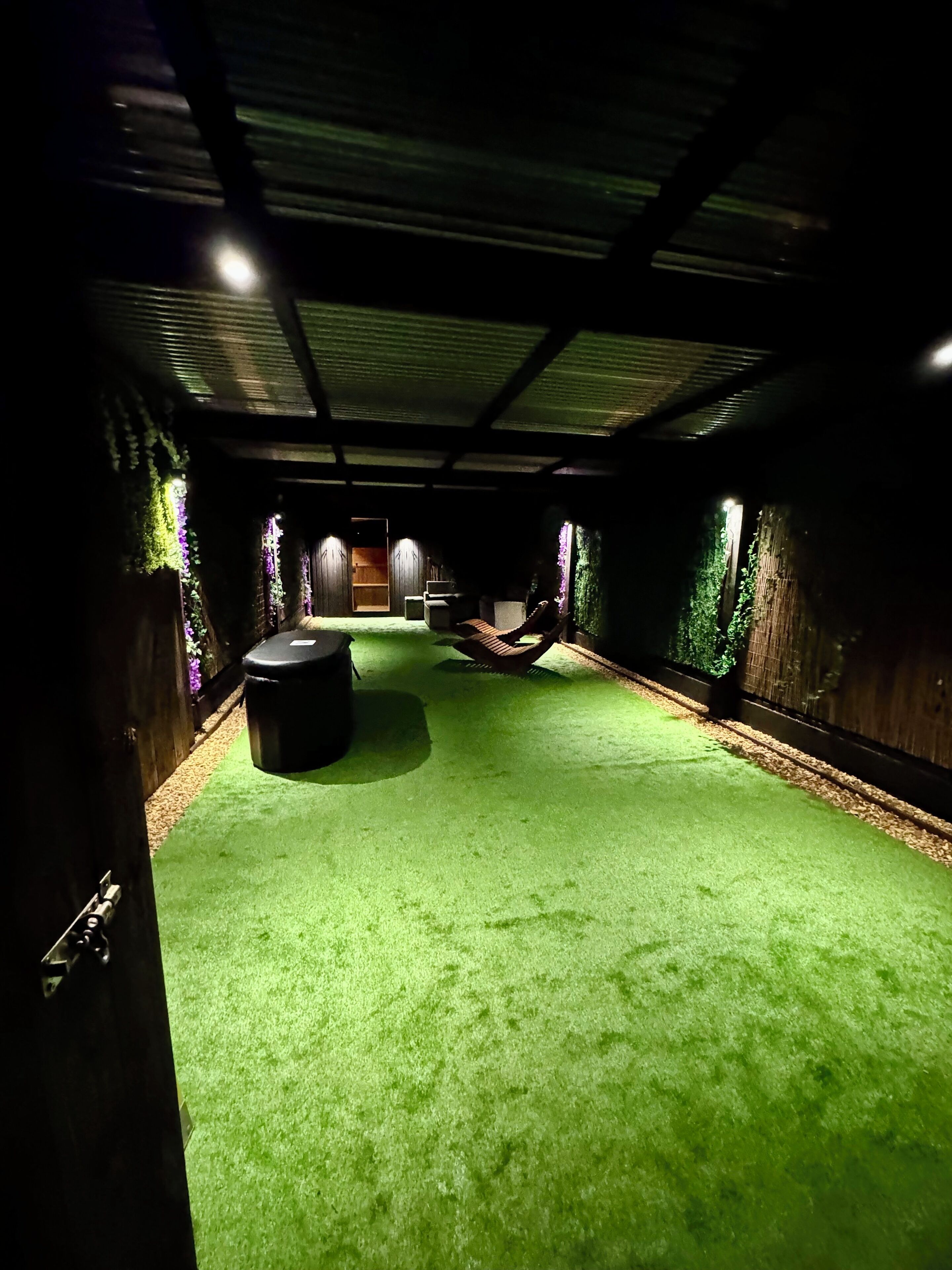 Una habitación con césped artificial verde, una hamaca y paredes de madera.