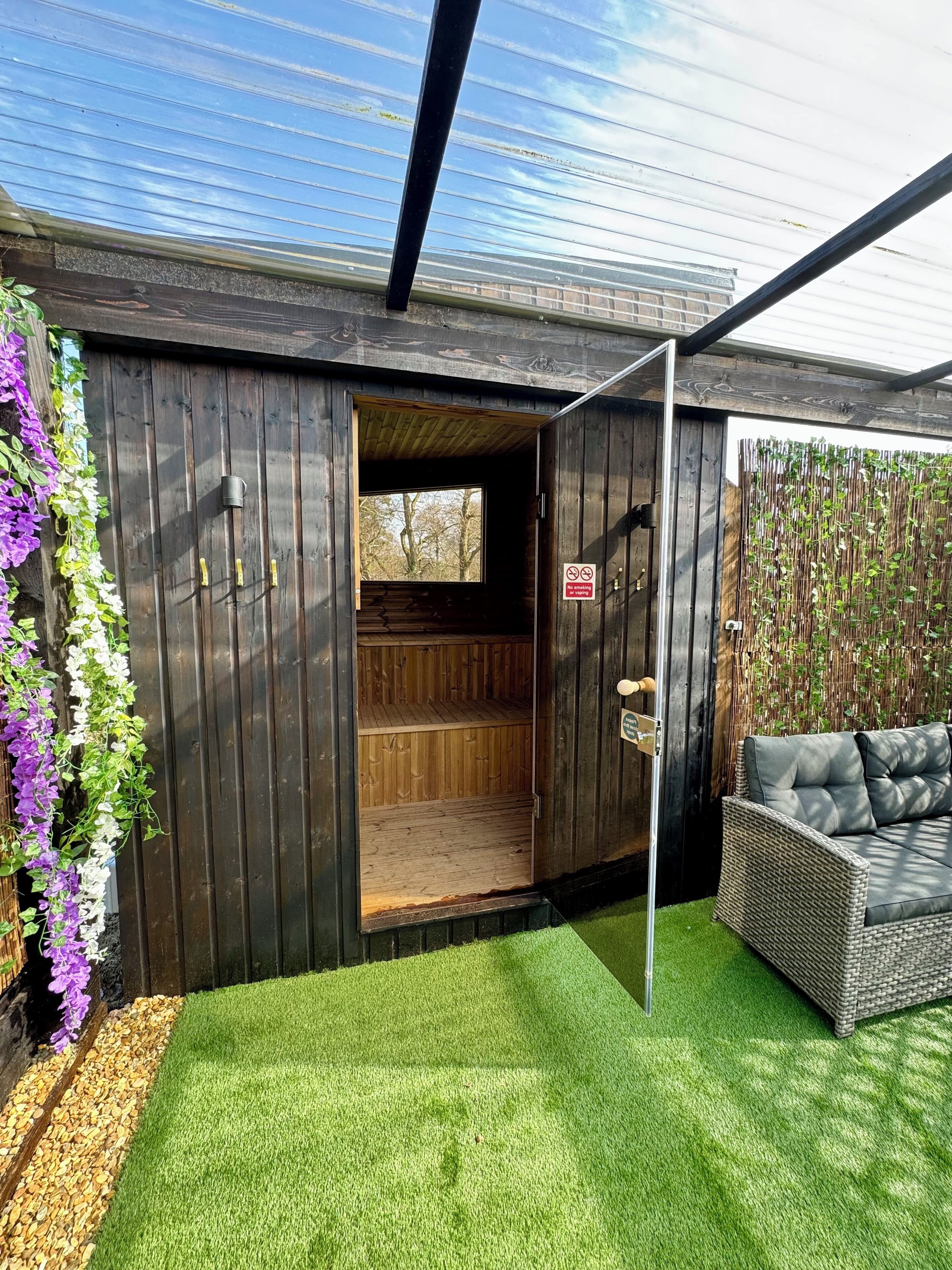 A wooden structure with a door leading to an interior space, a wicker sofa, and a vertical garden.