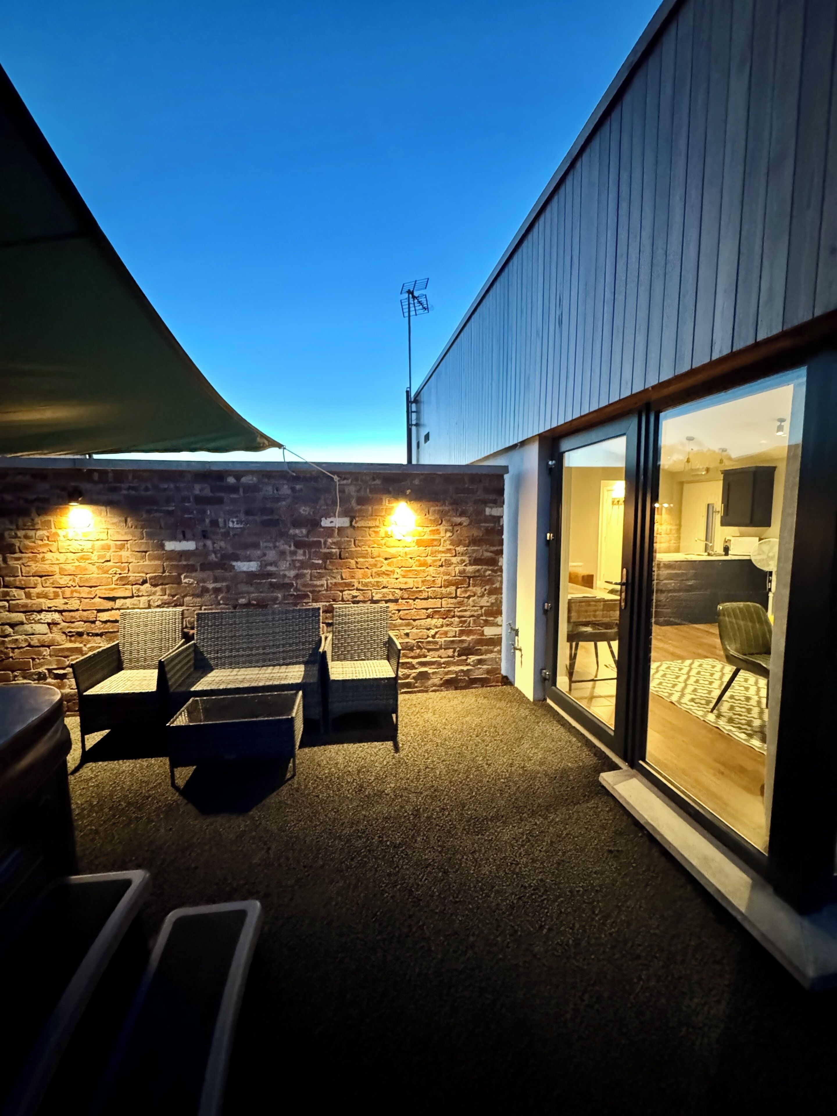 A patio area with wicker furniture and a brick wall, leading to a glass door entrance.