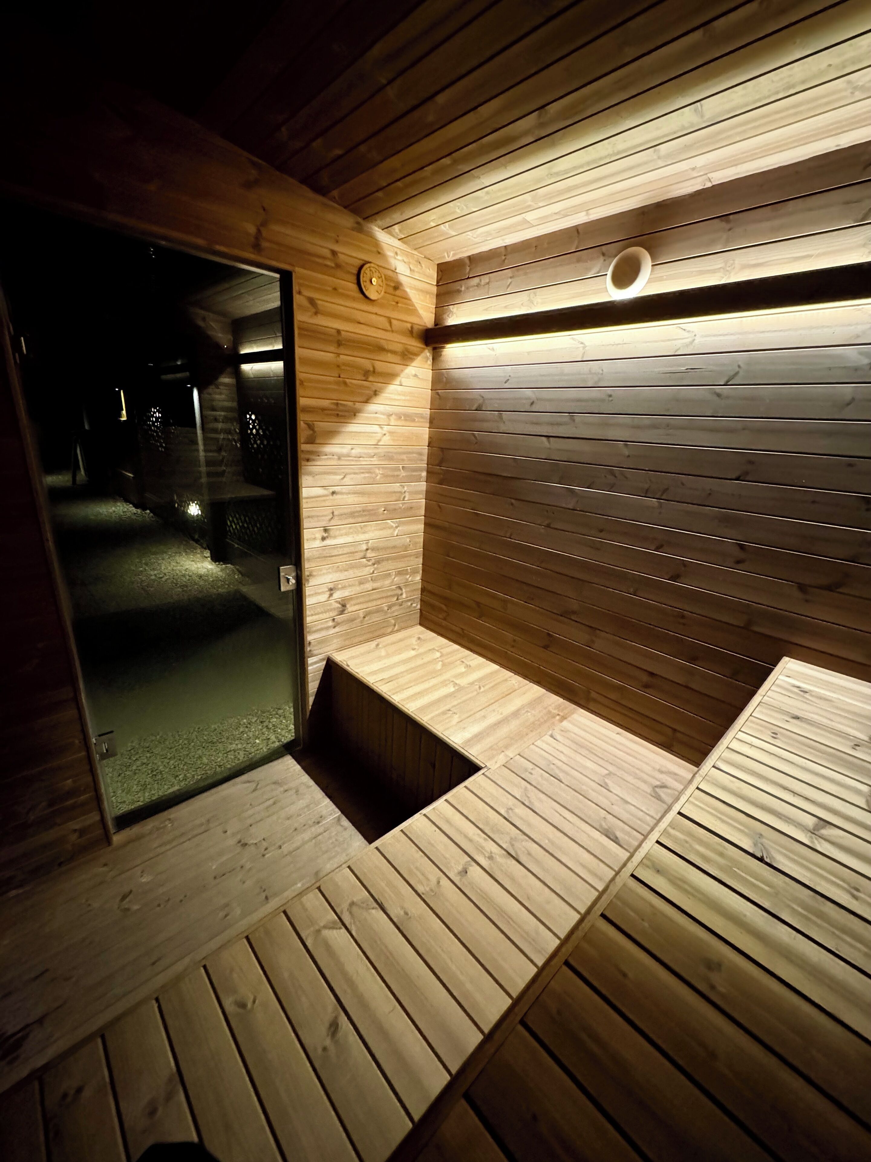 A sauna with wooden walls and benches, a door, and a small window.