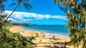 A beach with clear blue water, people sunbathing, and palm trees. - 180° Ocean views • Luxe condo • Steps to Beach (Kihei)