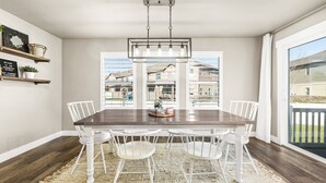 A dining room with a dark wooden table, white chairs, a woven rug, and a hanging light fixture.