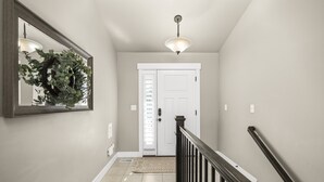 A hallway with a wooden railing, a white door, a light fixture, and a mirror with a wreath.