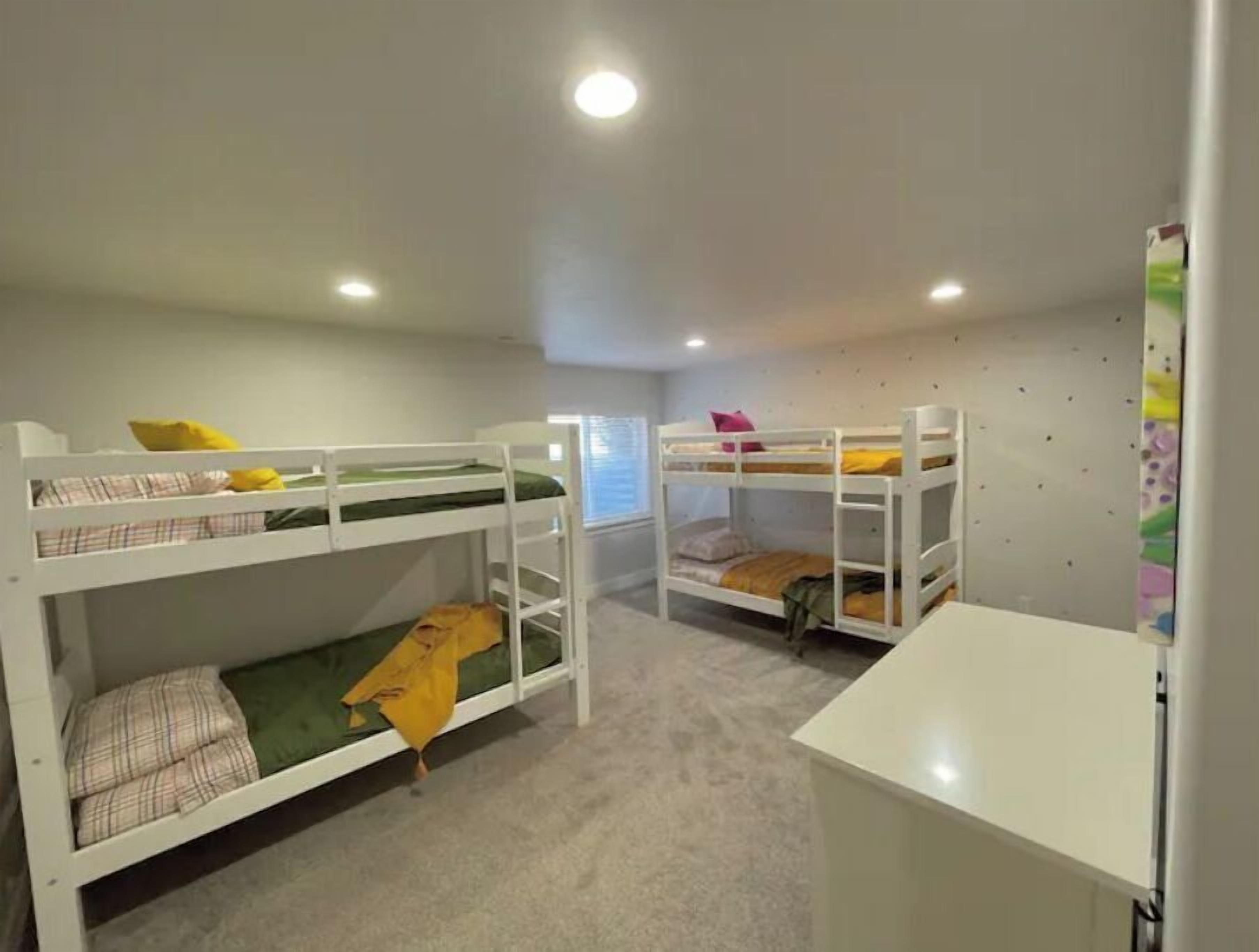 Une chambre avec deux lits superposés, un bureau blanc et une fenêtre avec des stores.