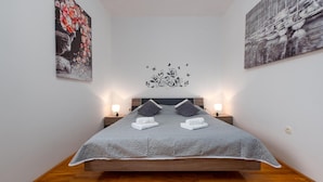 A neatly made bed with a grey quilt, two pillows, and two white towels. There are two bedside tables with lamps, and a decorative wall decal above the bed. - Awesome apartment in Privlaka with WiFi (Privlaka)