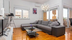 A modern living room with a grey sectional sofa, a glass coffee table, a black floor lamp, and a large window with a view of the outside. - Awesome apartment in Privlaka with WiFi (Privlaka)