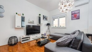 A modern living room with a flat-screen TV, a glass coffee table, a grey sofa, and a chandelier. - Awesome apartment in Privlaka with WiFi (Privlaka)