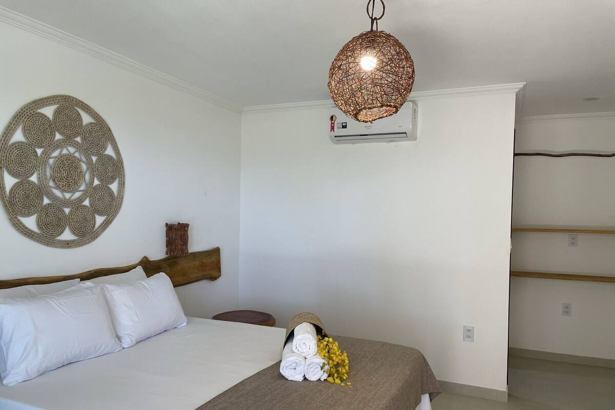 A bedroom with a bed, a decorative wall hanging, a hanging light fixture, and an air conditioning unit.