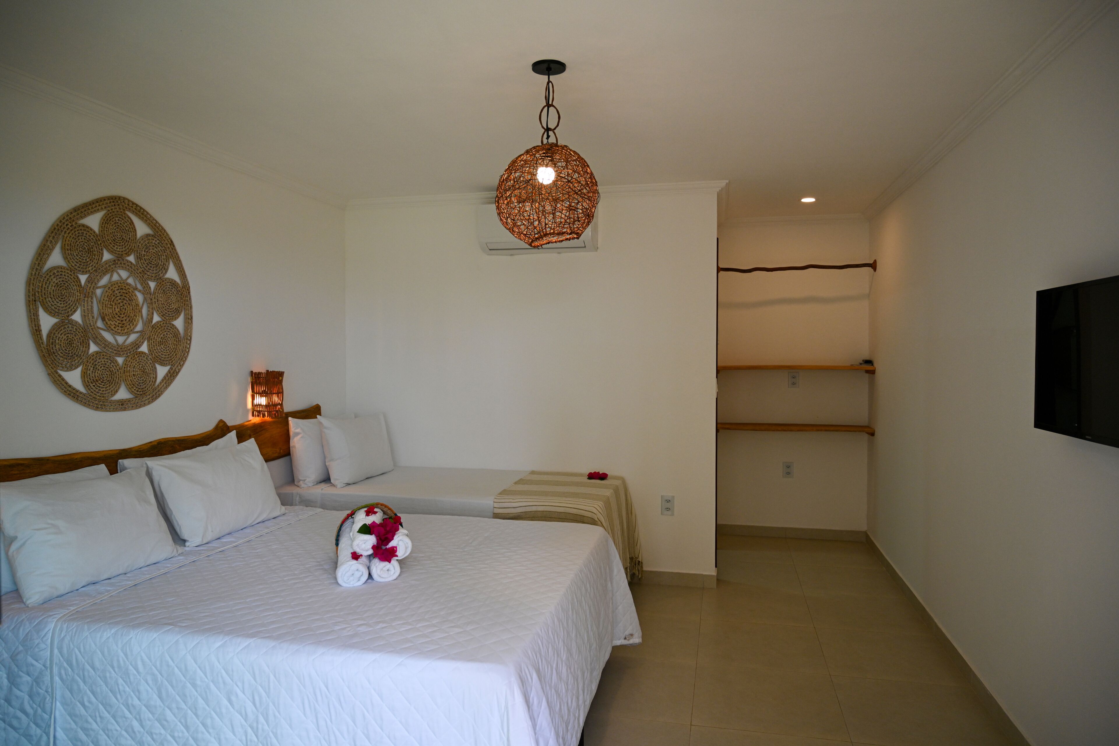 Habitación de hotel con dos camas, un tapiz decorativo, una lámpara colgante y un televisor montado en la pared.