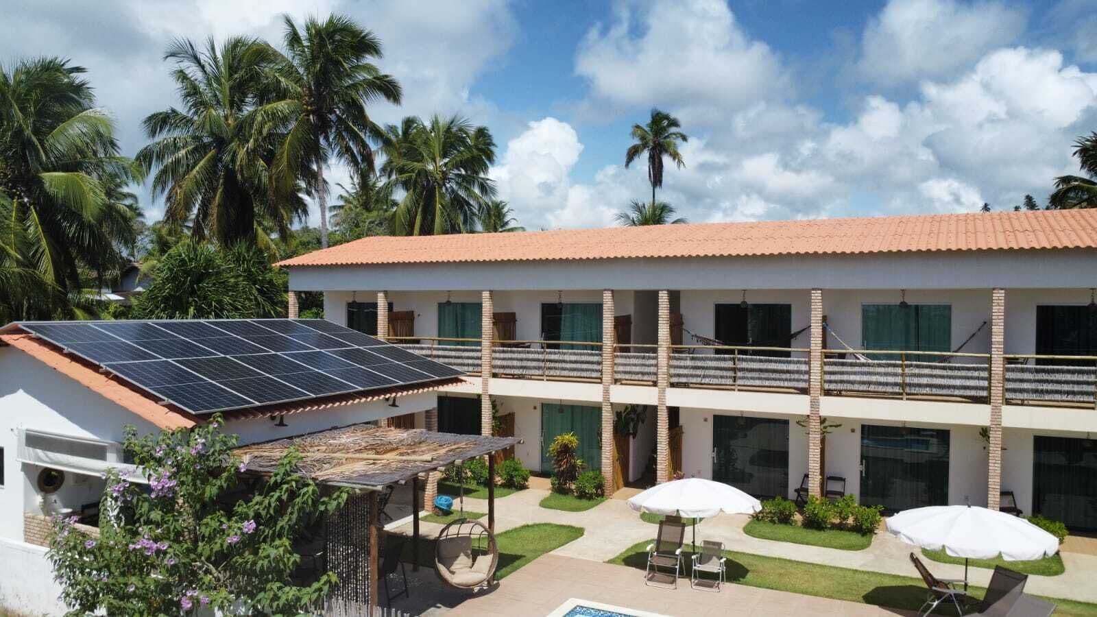 A two-story building with a tiled roof, a covered outdoor seating area, and a solar panel array.