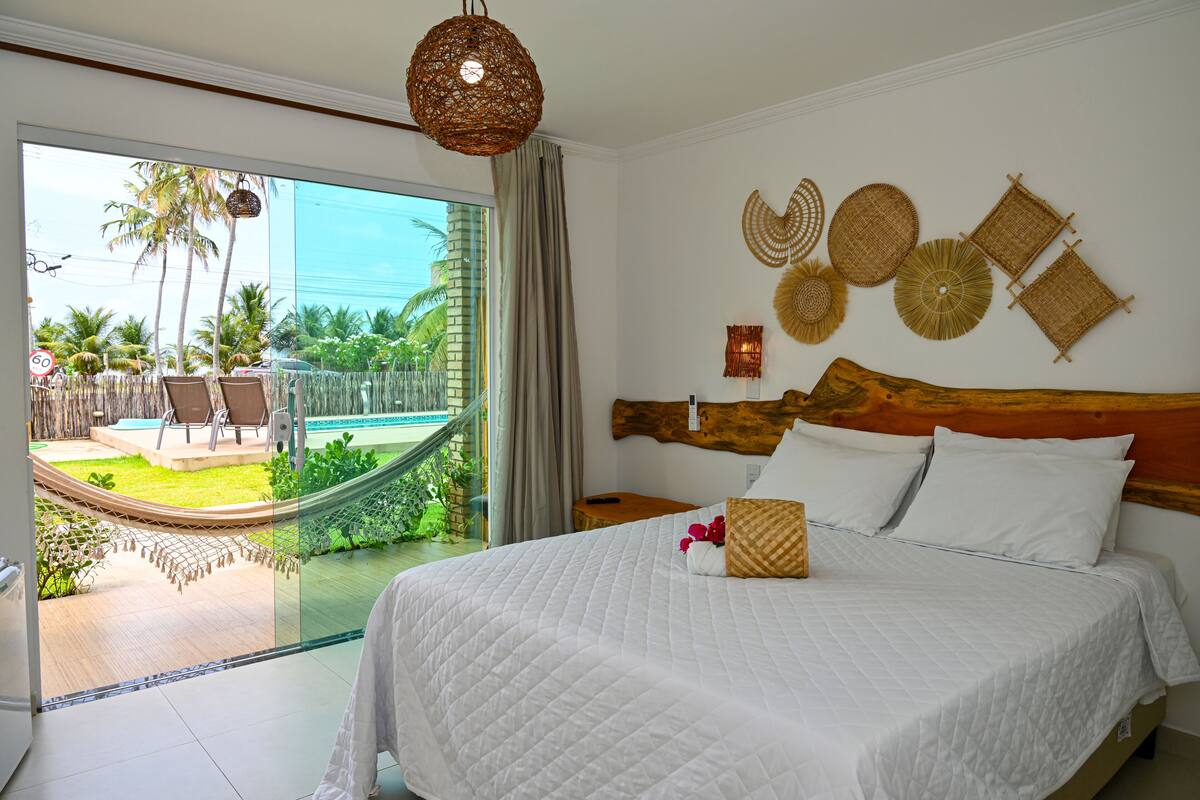 A hotel room with a large bed, a wooden headboard, and a view of a pool and palm trees.