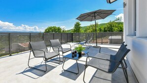 Un balcon avec quatre chaises, une table et un grand parasol.