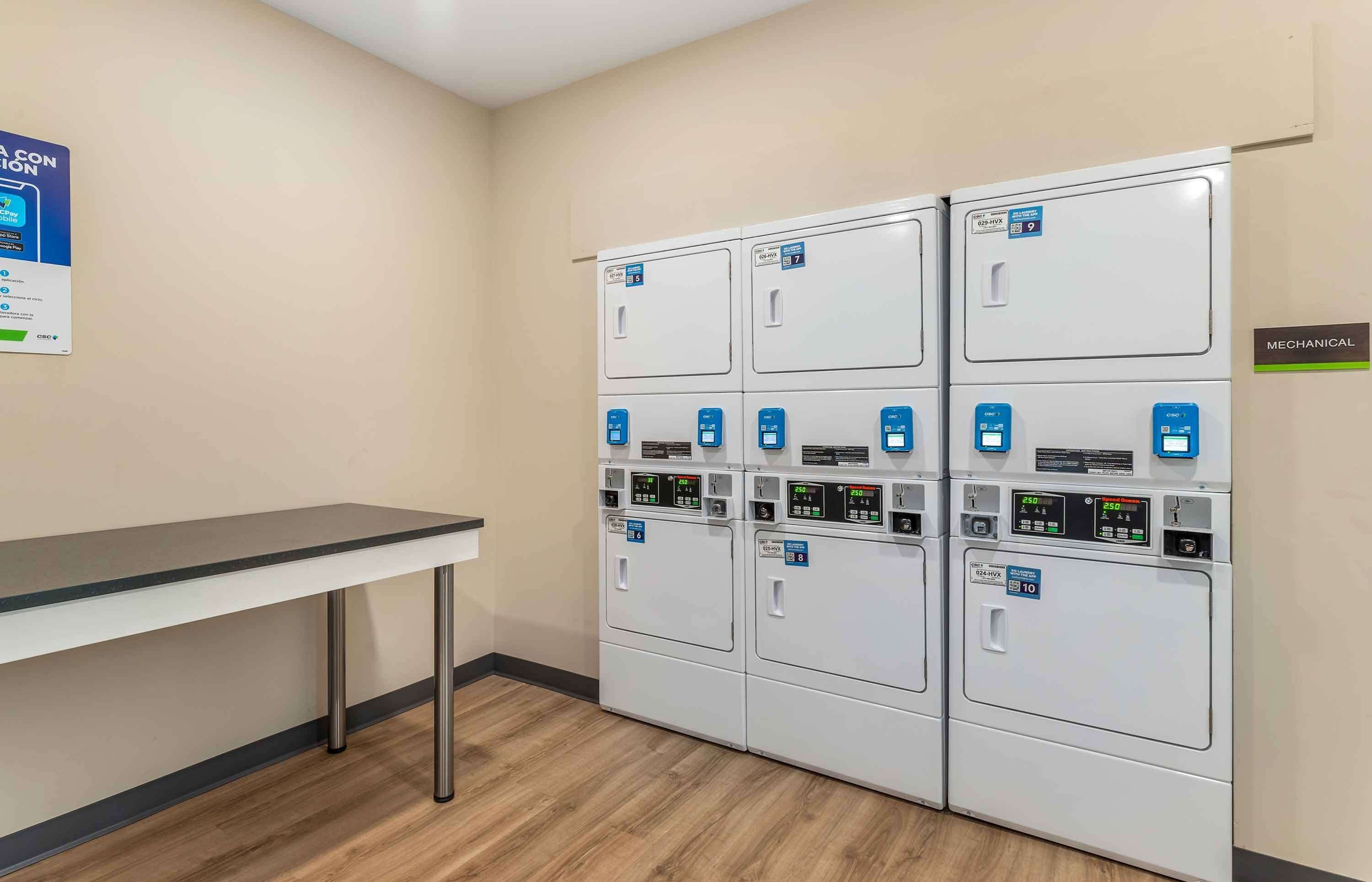 A laundry room with four stacked washing machines, a table, and a sign indicating the mechanical room.