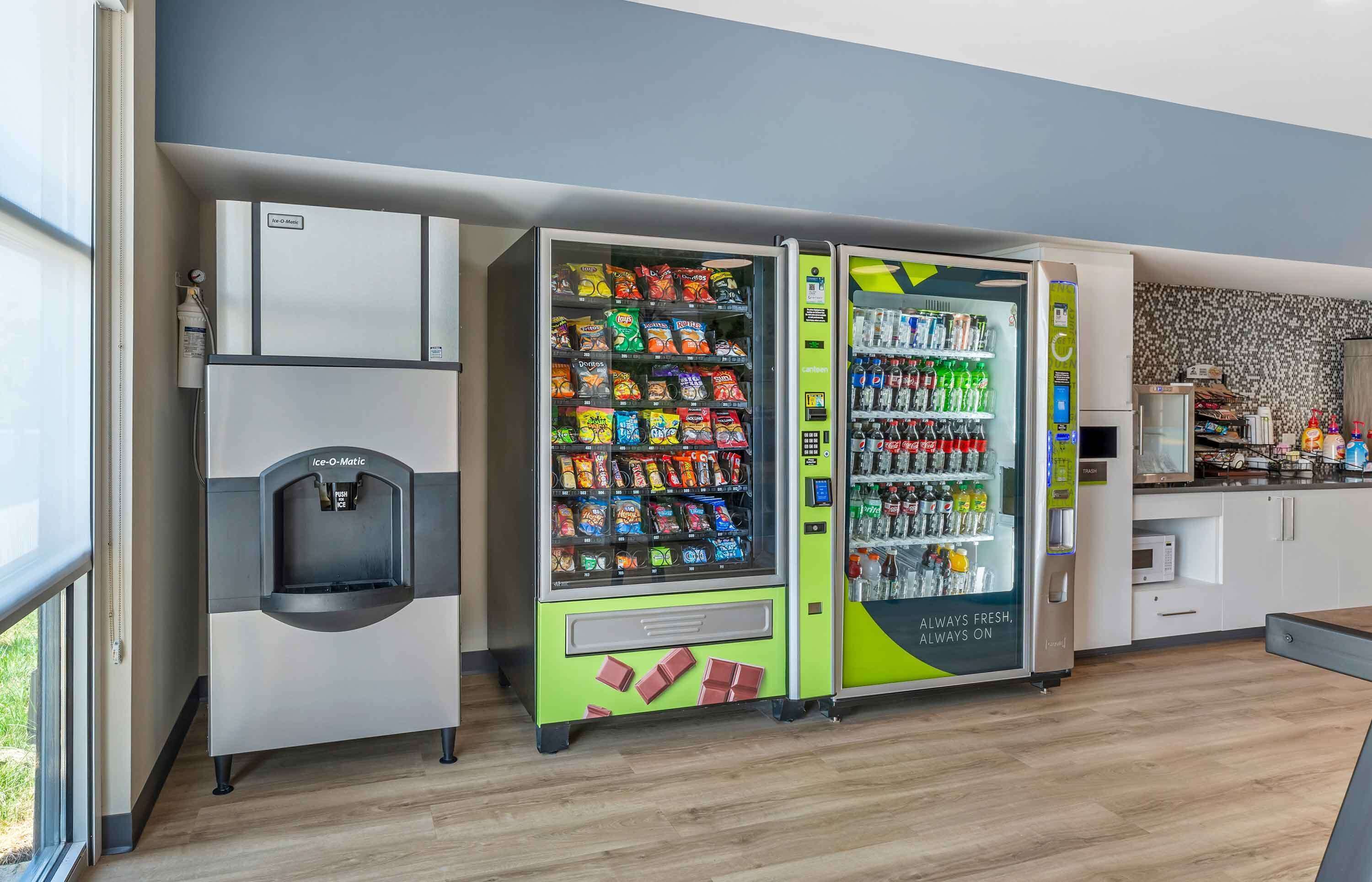 A modern kitchen with a vending machine selling snacks and beverages, a water dispenser, and a microwave.