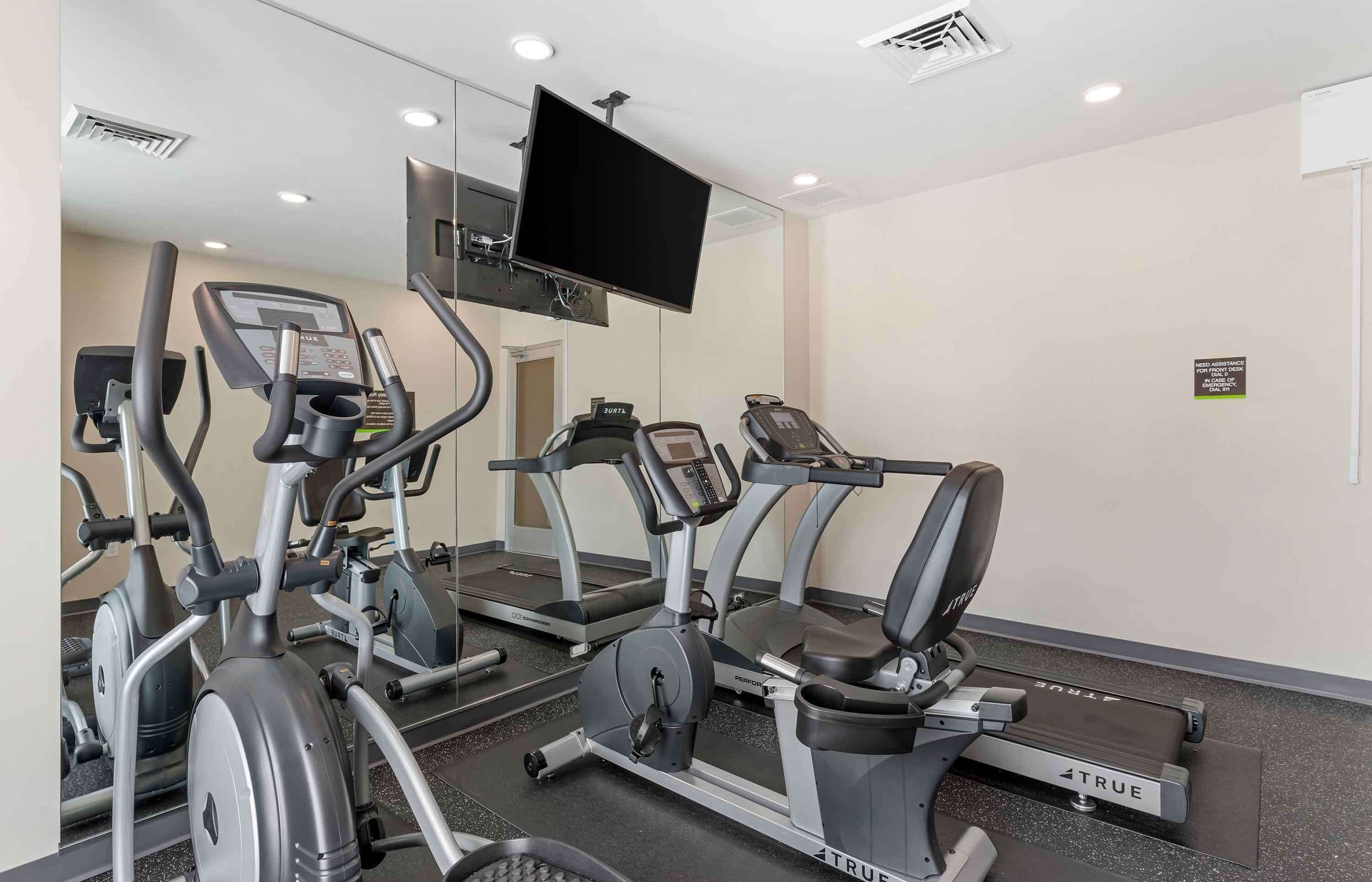 A gym with various exercise machines, a large mirror, and a mounted TV.