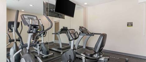 A gym with various exercise machines, a large mirror, and a mounted TV.