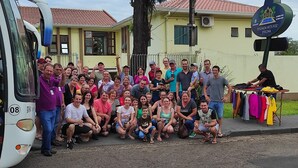 A group of people posing in front of a bus and a building with a sign that reads "Ousada Hits Foz Evelina." - Pousada Hits Foz (Foz do Iguaçu)