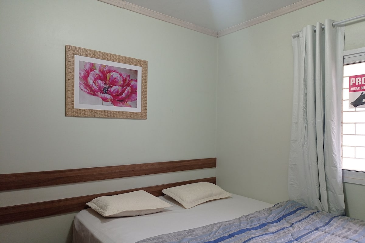A bedroom with a bed, pillows, a framed picture on the wall, and a window with curtains.