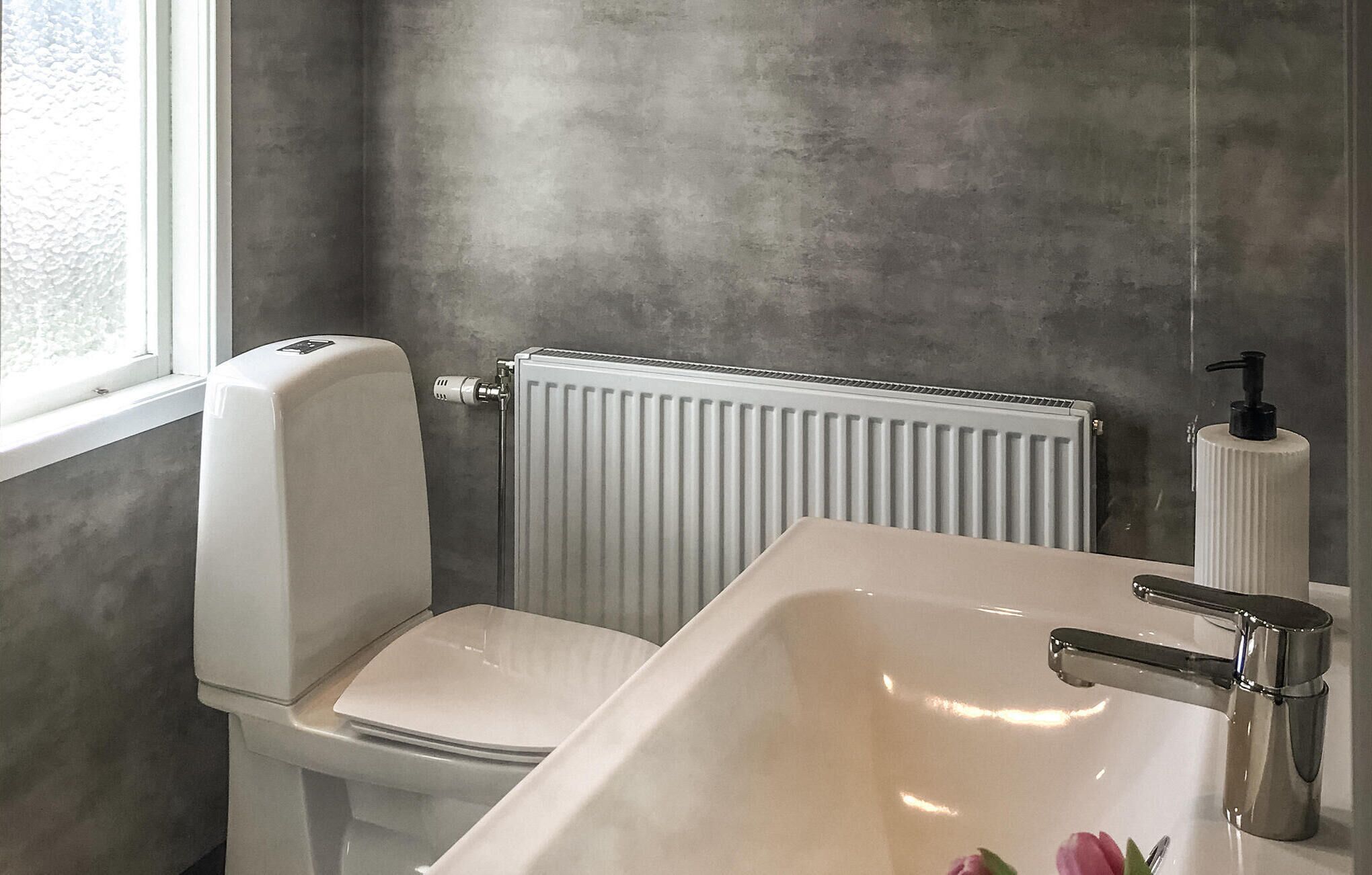 Une salle de bain comprenant des toilettes, un lavabo, un radiateur et une fenêtre.