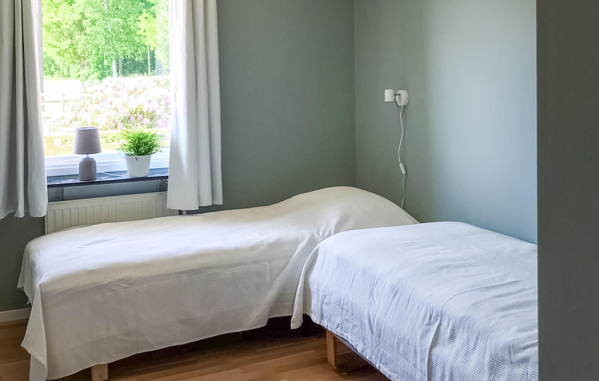 Une petite chambre individuelle avec deux lits simples, une fenêtre avec des rideaux, un radiateur et une prise électrique au mur.