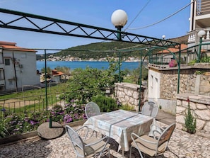 A terrace with a table and chairs, overlooking a coastal town and a body of water.